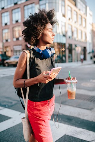 Woman walking in the city, holding a drink and her phone
