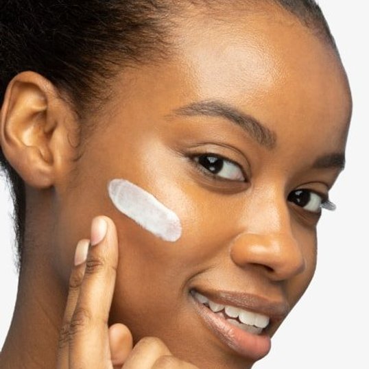 close up of woman’s face applying moisturiser for a glowy clean girl look