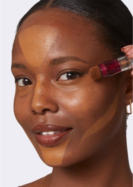 close-up of woman’s face as she applies concealer for a clean girl makeup look