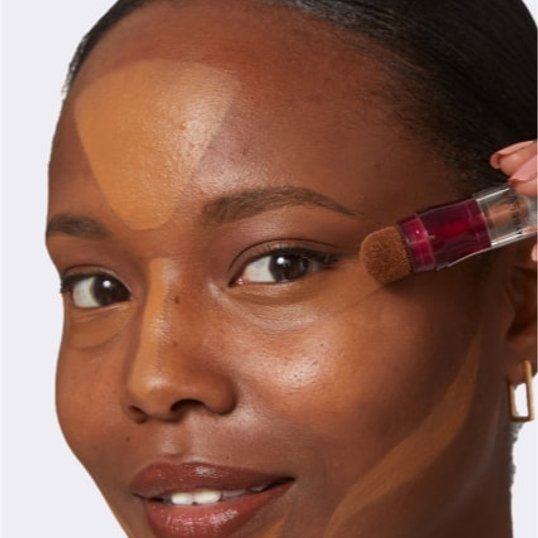 close-up of woman’s face as she applies concealer for a clean girl makeup look