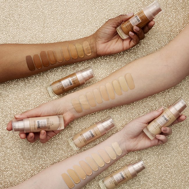 A shot of 3 women’s arms, all with different skin tones, showing how the various shades of Maybelline’s Dream Radiant Liquid Foundation complement different skin tones.