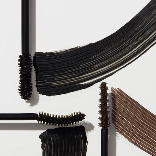 Promotional shot showing Maybelline black and brown mascara wands drawing black and brown coloured lines, with text at the bottom reading: MAYBELLINE MAKEUP DECODED.