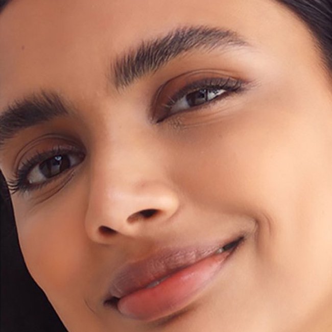 A close-up of a smiling woman with subtle makeup on including fluffy brows, brown eyeliner, and perfectly matched foundation