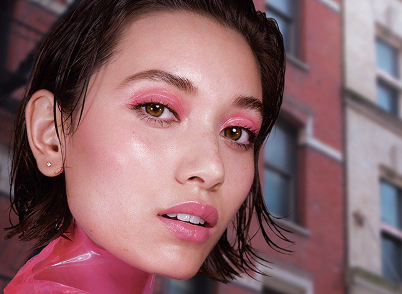 A model wearing pink eyeshadow and Maybelline setting spray looks into the camera.