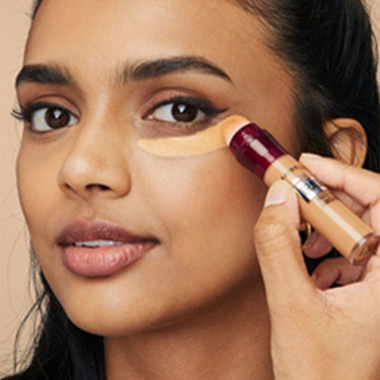 A woman applies a yellow colour corrector to the area underneath her eye.